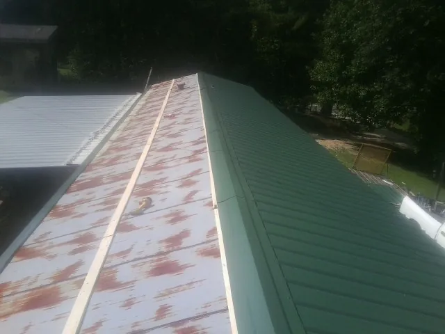 Old rusted panels beside newly installed green metal roofing — Wind Damage Roof Repair by Roofing Brothers in Linville