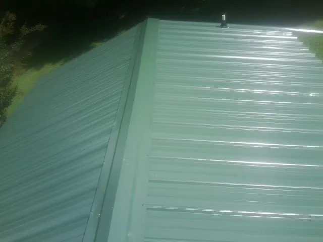 New green metal panels meeting at the ridge of a roof — Flat Roof Repair work by our crew in Linville