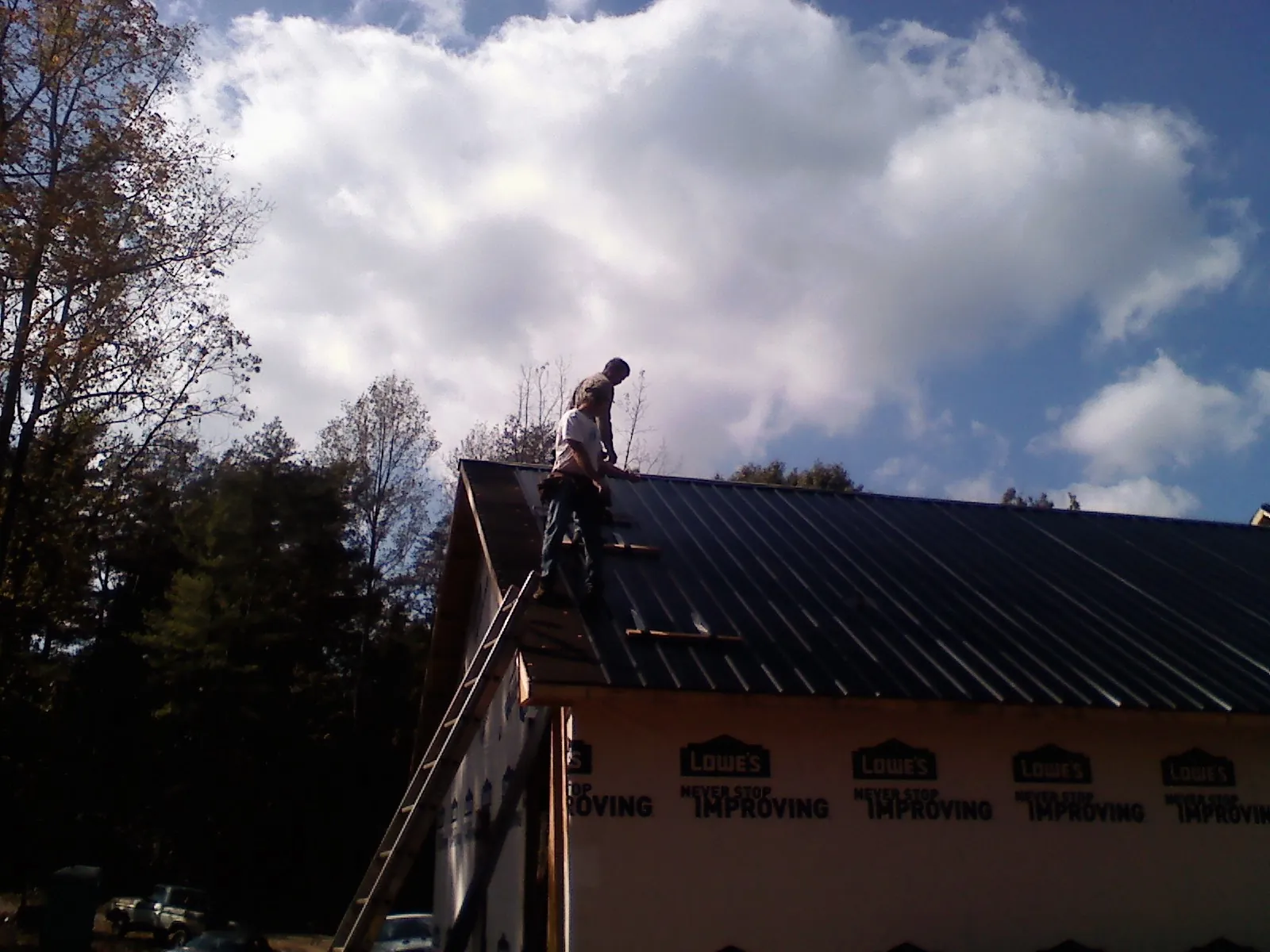 Roofer fastening dark metal panels high against a cloudy sky, from a Roof Inspection job in Linville